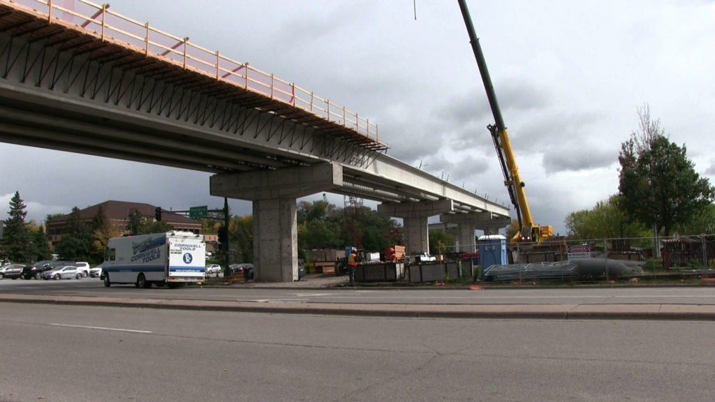 A scene of a road and an overhead bridge. The scene shows some cars and vans on the road