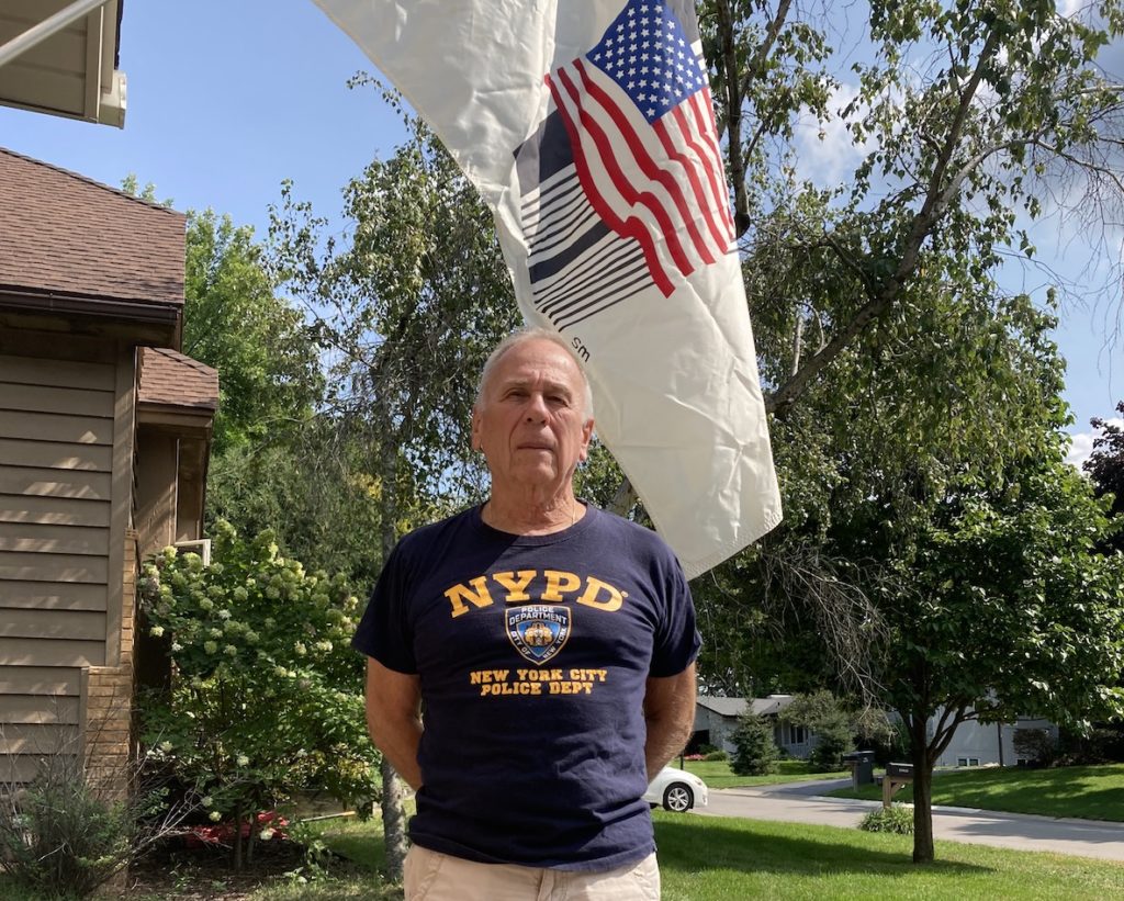 Man stands near flag with NYPD shirt on.