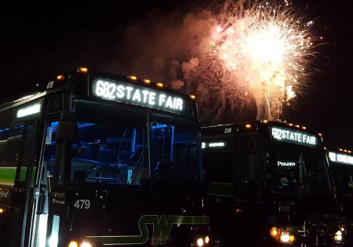 Buses idle in front of the fireworks lighting up the dark sky.