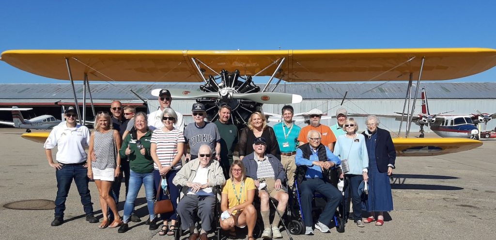 Group shot of the veterans, family and friends in front of vintage yellow airplane