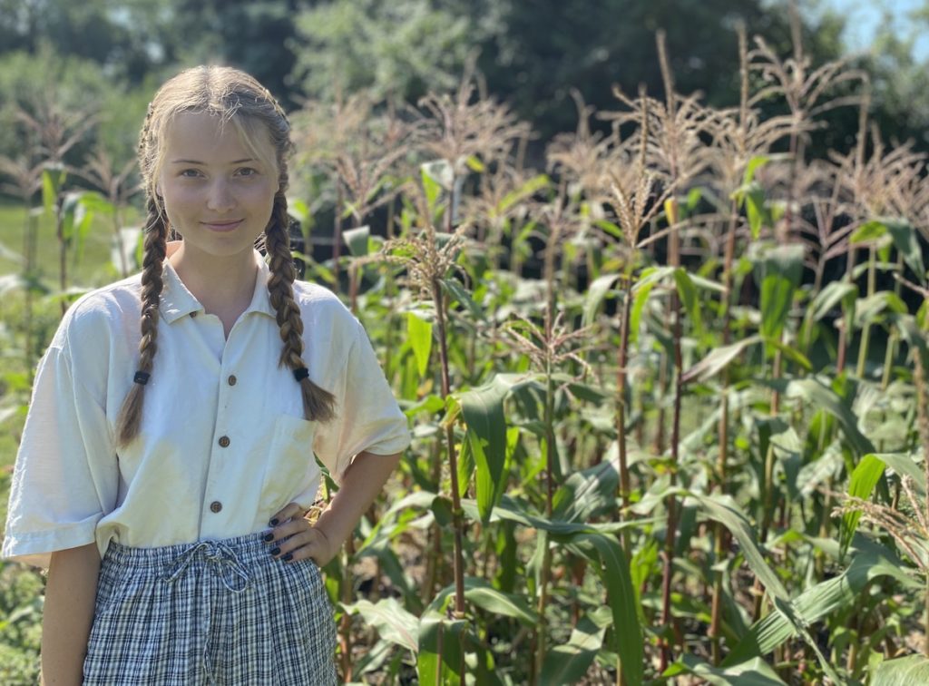Calista Swensen stands in the garden, her left hand resting on her hip.