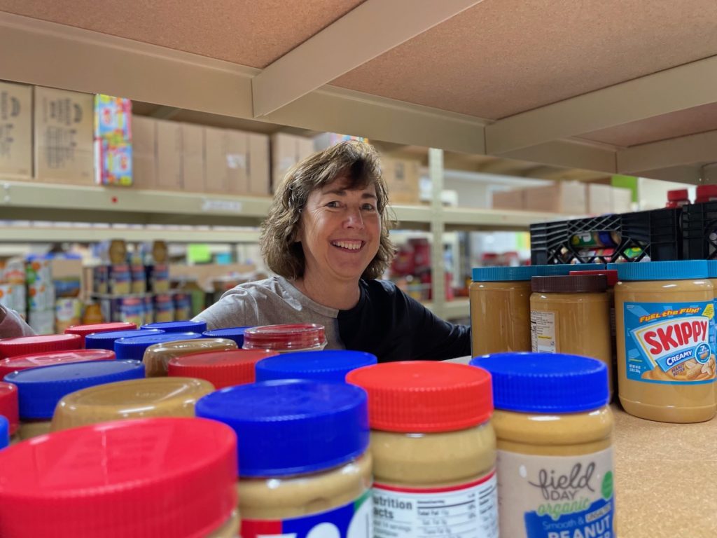 Janet Palmer poses in the PROP Food Shelf, behind jars of peanut butter.
