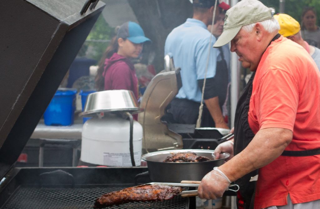 A man grabs turns over a rack of ribs on a large grill.