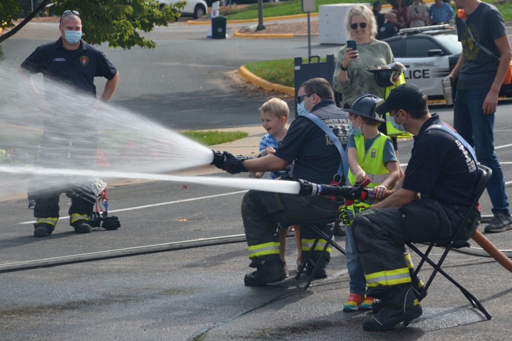 A boy gets a little help holding a fire hose.