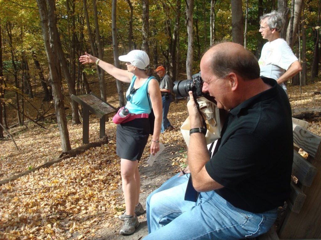 A man takes a photo in the Richard T. Anderson Conservation Area while a woman talks about the big woods forest there.
