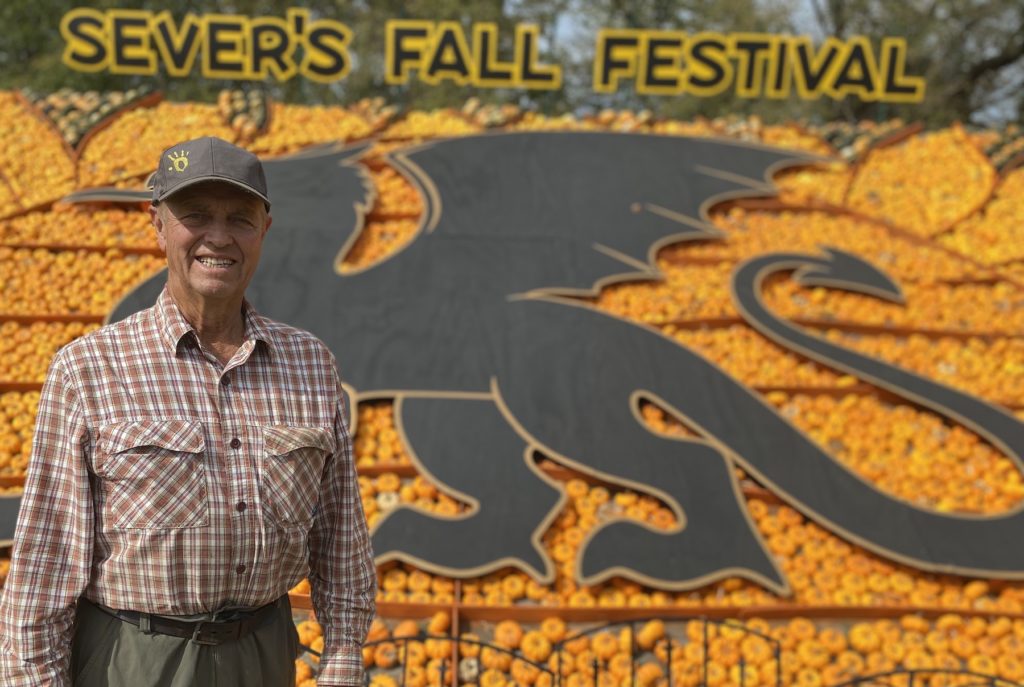 Sever Peterson stands in front of a large dragon cutout surrounded by colorful pumpkins, gourds and squash.