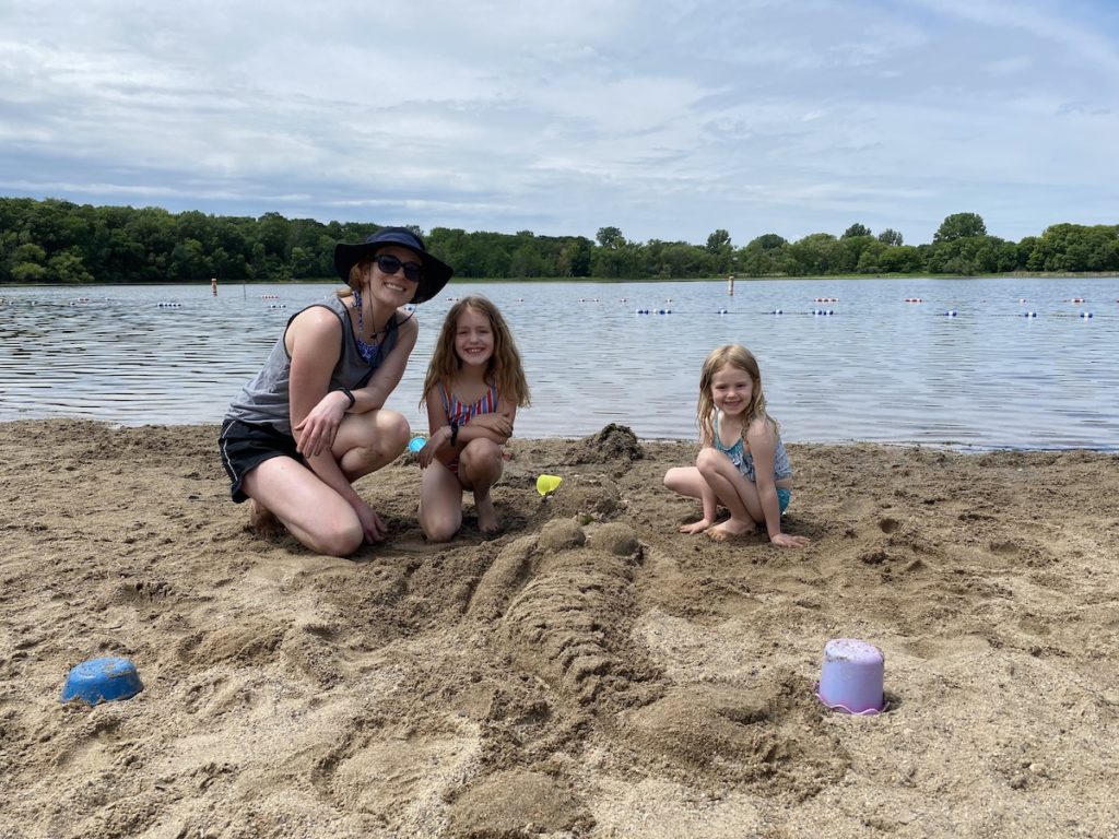 Girls just wanna have sun: Round Lake beachgoers Lindsey, Marion, and Hannah Meyer, along with their sand creation, Fiona Marina Mermaid. Photos by Juliana Allen