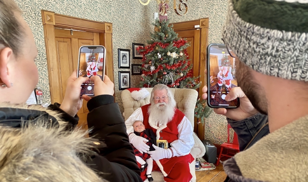 Talia Schmidt of Hampton, Iowa, and Aaron Aldridge of Eden Prairie snap photos with their phones of baby Ava Aldridge with Santa Claus at the Cummins-Phipps-Grill House in Eden Prairie on Saturday. Talia, her husband Jon and daughter Gemmaline were visiting friends Aaron and his wife Liz  in Eden Prairie last weekend. Photos by Stuart Sudak