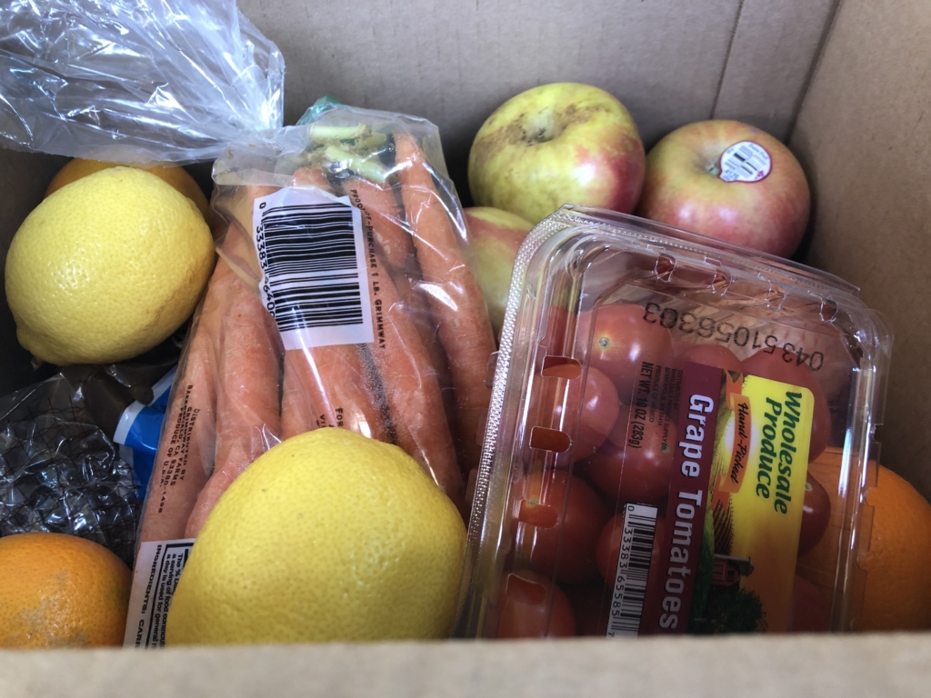 food including lemons, carrots, apples, tomatoes in cardboard box
