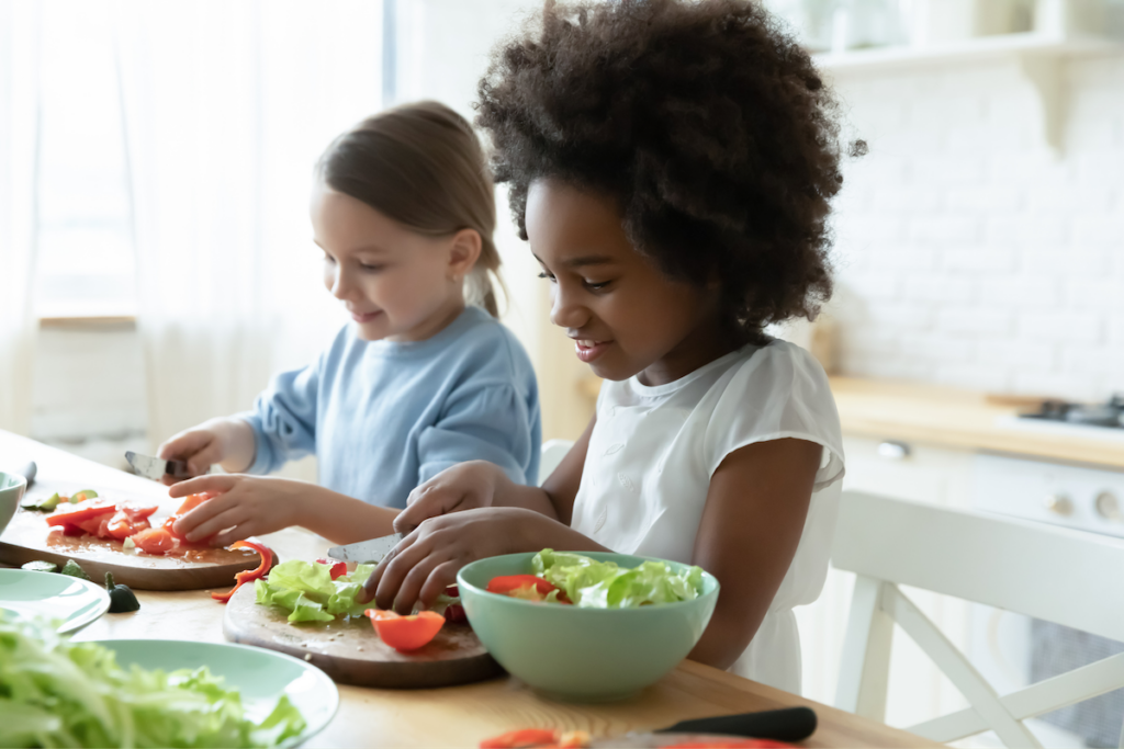 Two girls laugh while they make lunch.