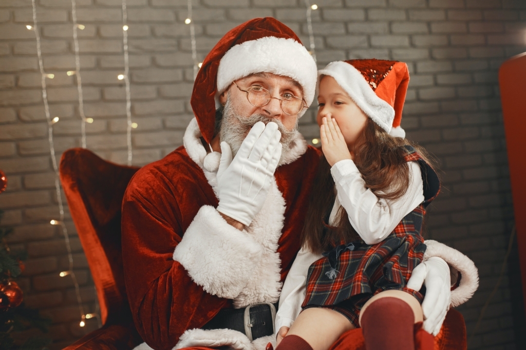 Santa with little girl in his lap whispering in his ear.