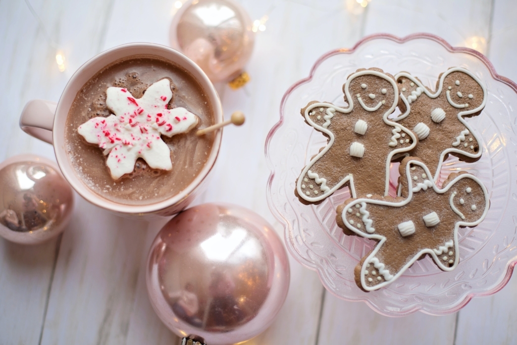 A glass plate of gingerbread men cookies, a hot beverage with a snowflake cookie floating in the cup, and silver Christmas ball ornaments