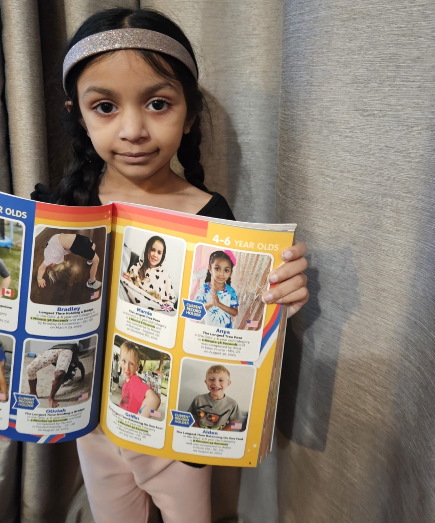 little girl wearing silver headband holds a book open to pages of world records for 4-6-year-olds
