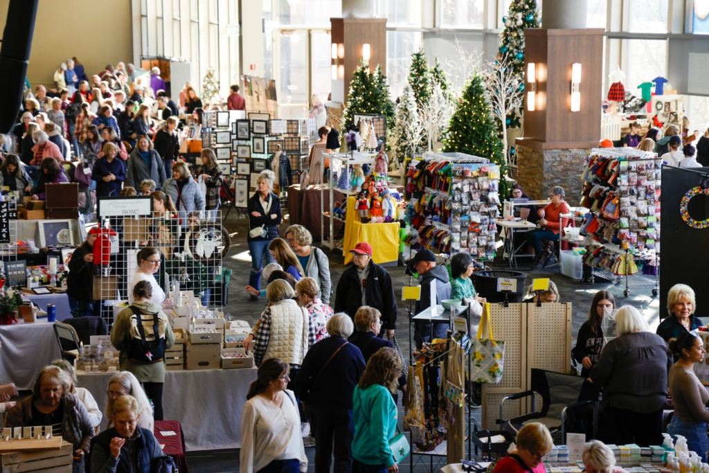View from above of shoppers at booths at a craft show, Christmas trees visible