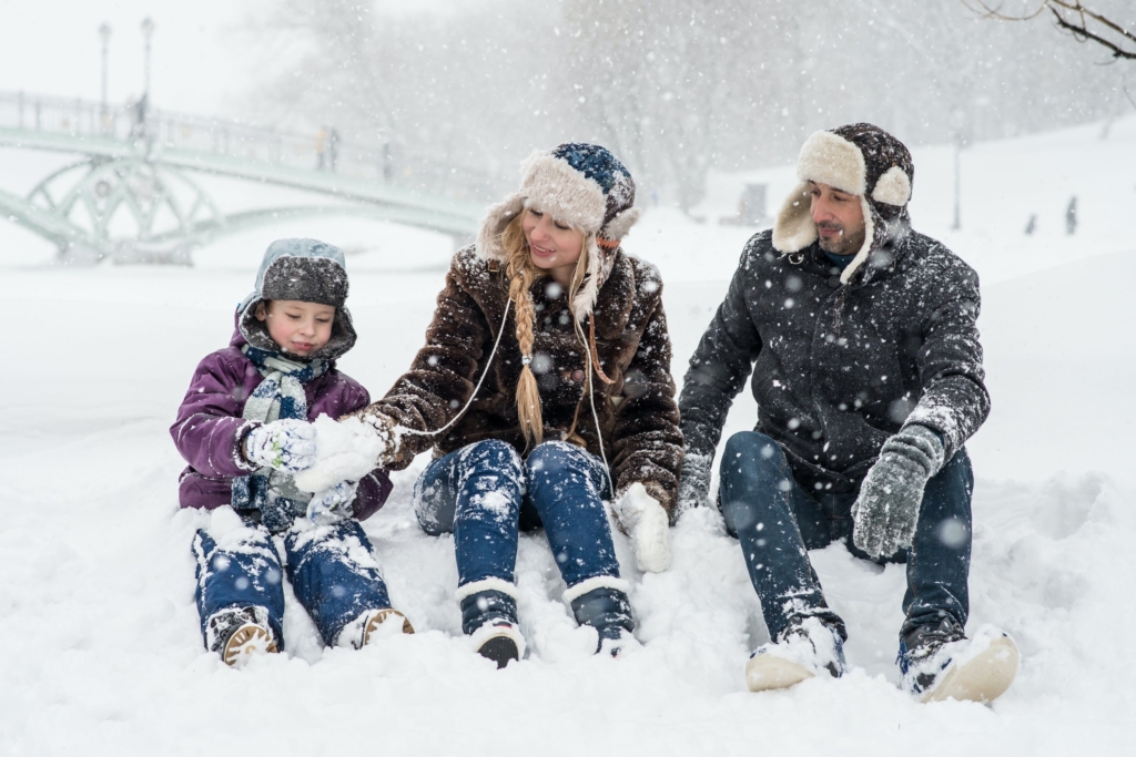 Child, woman, and man sitting on snow.