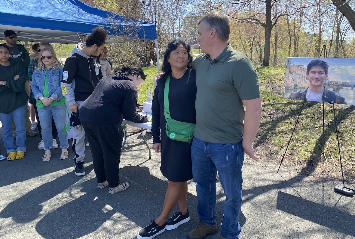 Thuy and Jamey Husmann speak at a ribbon ceremony on Sunday afternoon in front of a photo of their son, Aaron, who died last year. The event honored Aaron's memory and promoted mental health awareness among students. Photo by Stuart Sudak