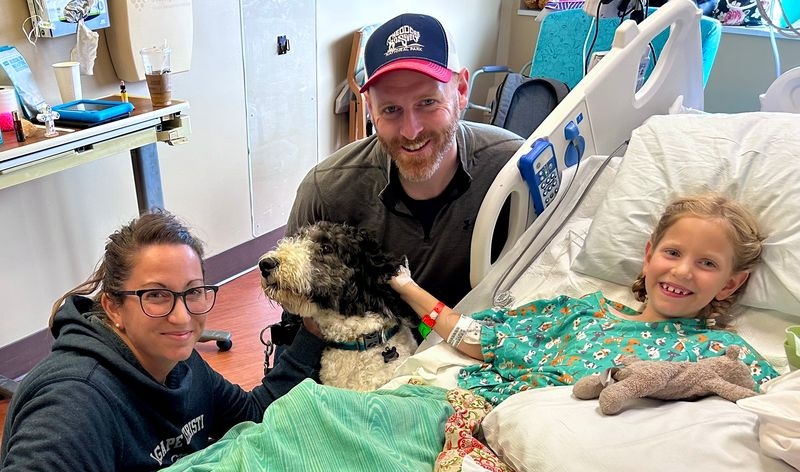 Selah Toney in the hospital with her parents, Kelina and Brett, and a very special visitor – Tumnus, her Sheepadoodle. Contributed photo
