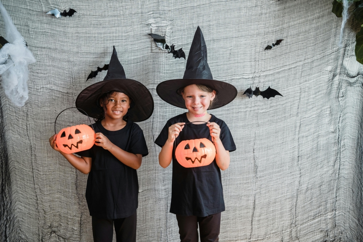 Two girls waering witches hats and carrying plastic Halloween pumpkins