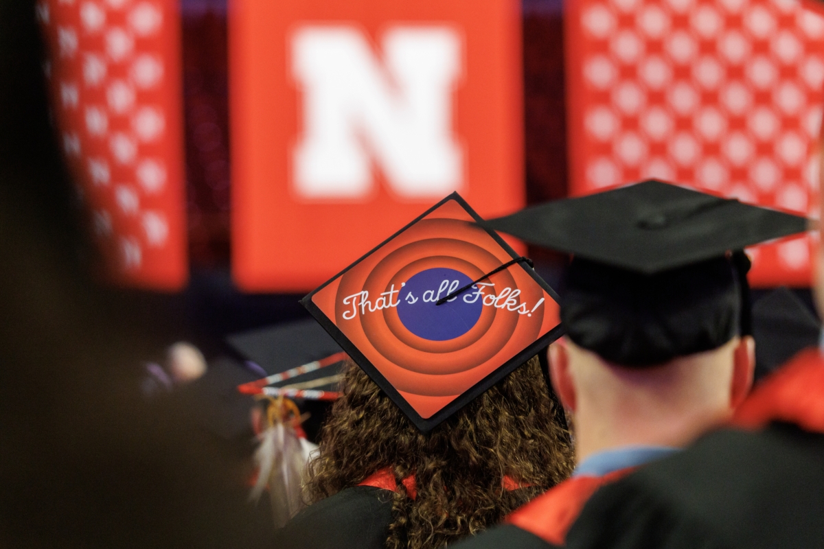 view of back of graduates' heads wearing mortarboards, with one saying "That's all folks" on the mortarboard