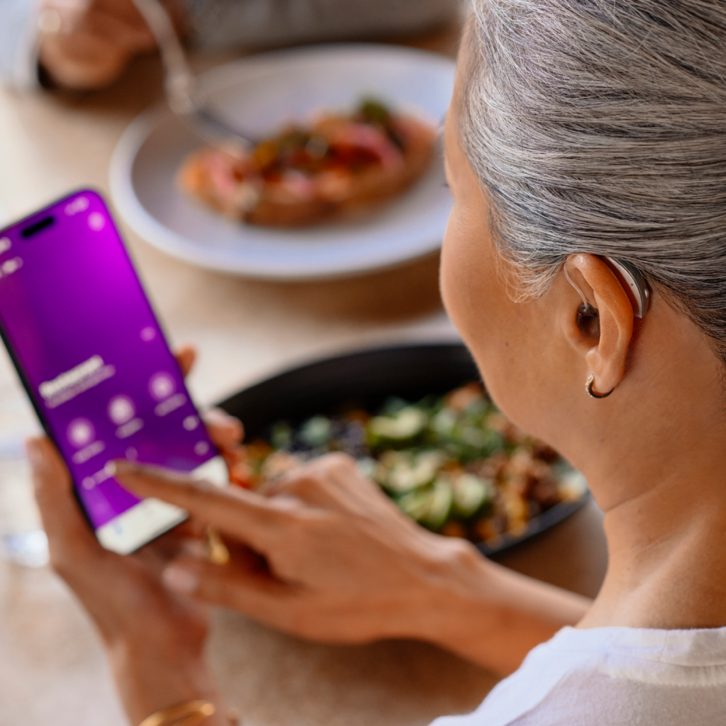 woman with hearing aid programming her smart phone while seated at restaurant table