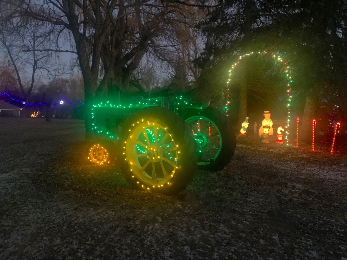 Farm tractor decorated with strings of green and yellow Christmas lights.