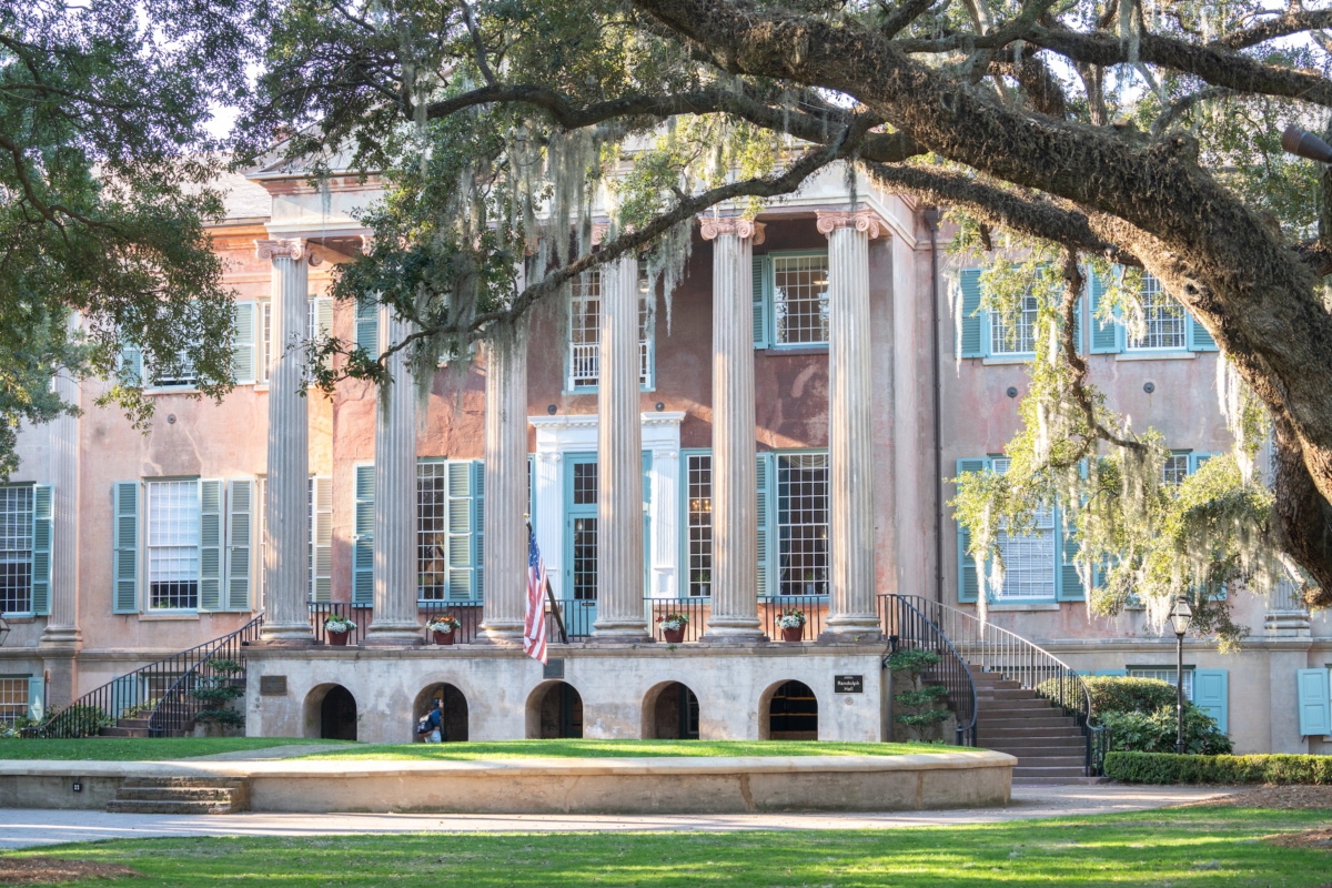 college building with columns and an American flag and tree in front on a sunny day