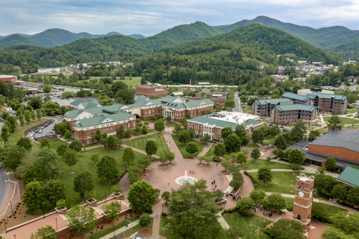 An aerial view of a college campus at foothills of wooded mountains.