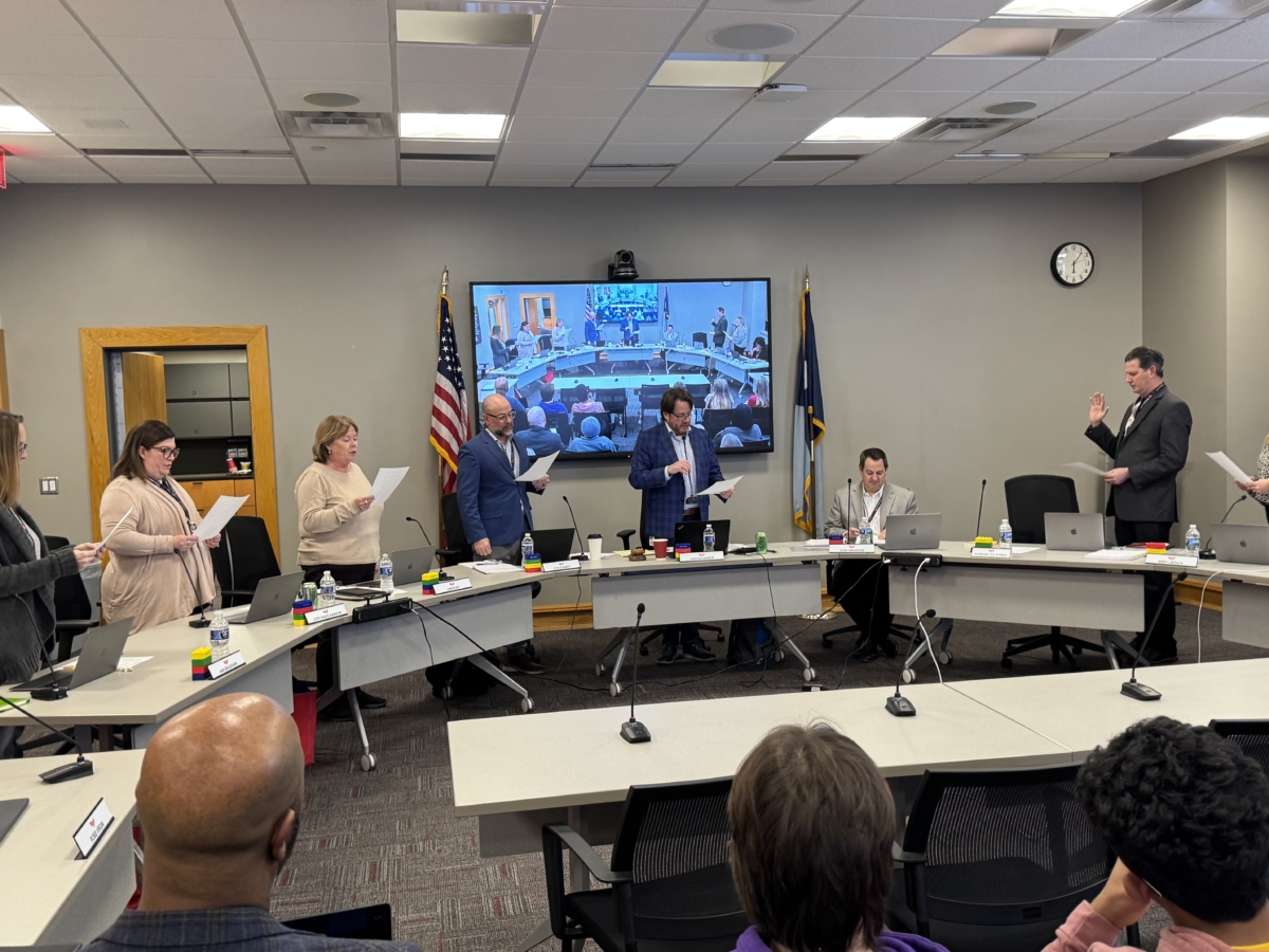 Eden Prairie School Board members reading the oath of office, as Charles "C.J" Strehl temporarily rejoins the board. (L-R) Ann Bradsher, Jody Ward-Rannow, Kim Ross, Steve Bartz, Aaron Casper, Superintendent Josh Swanson, Charles “CJ” Strehl, and Abby Libsack. Photo by Juliana Allen