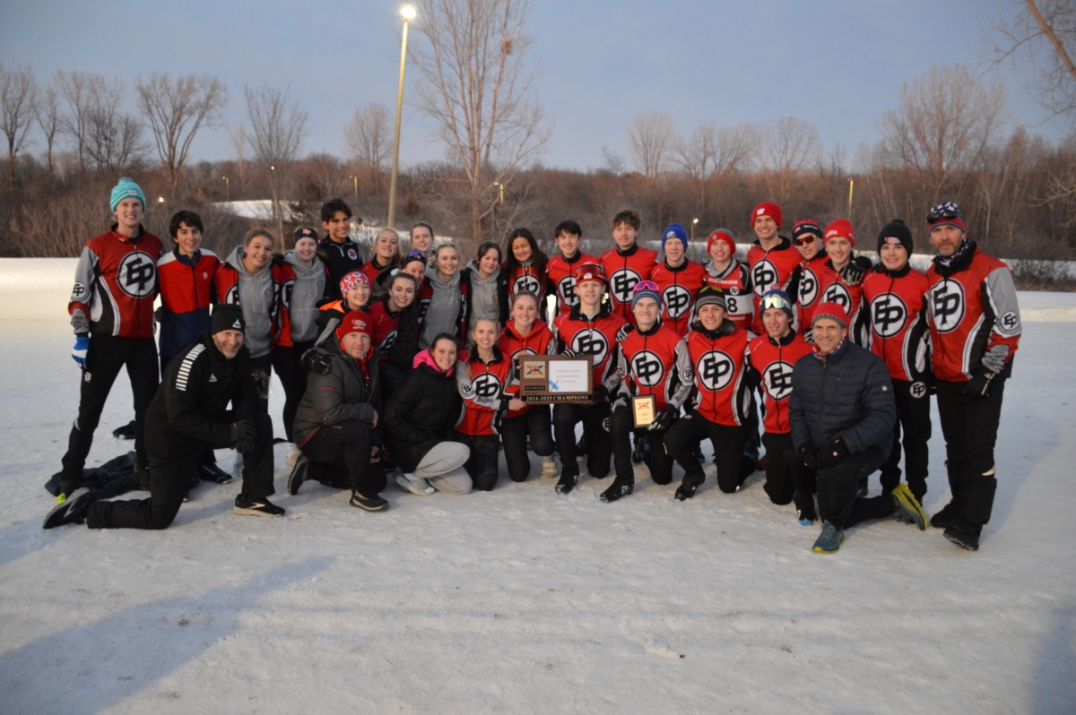 members of a cross country ski team with EP on their red and black uniforms pose for a team photo on a snow-covered field