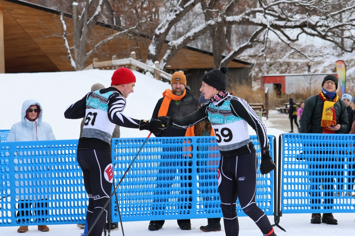2 skiers shake hands in front of blue net in front of onlookers