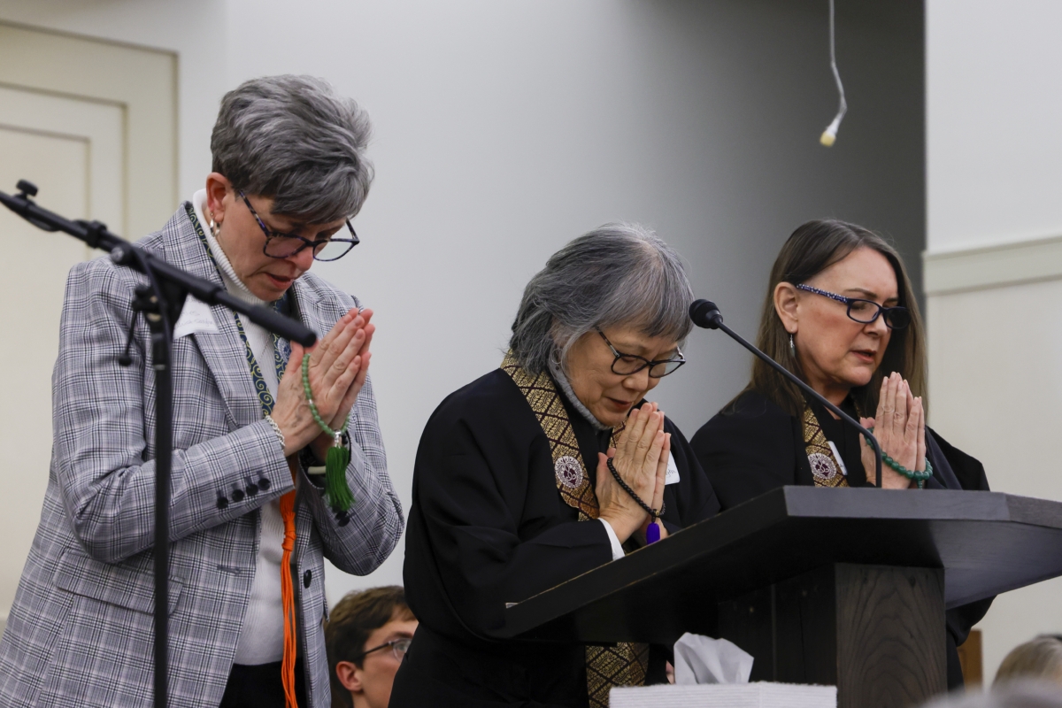 3 women with heads bowed and hands folded in prayer