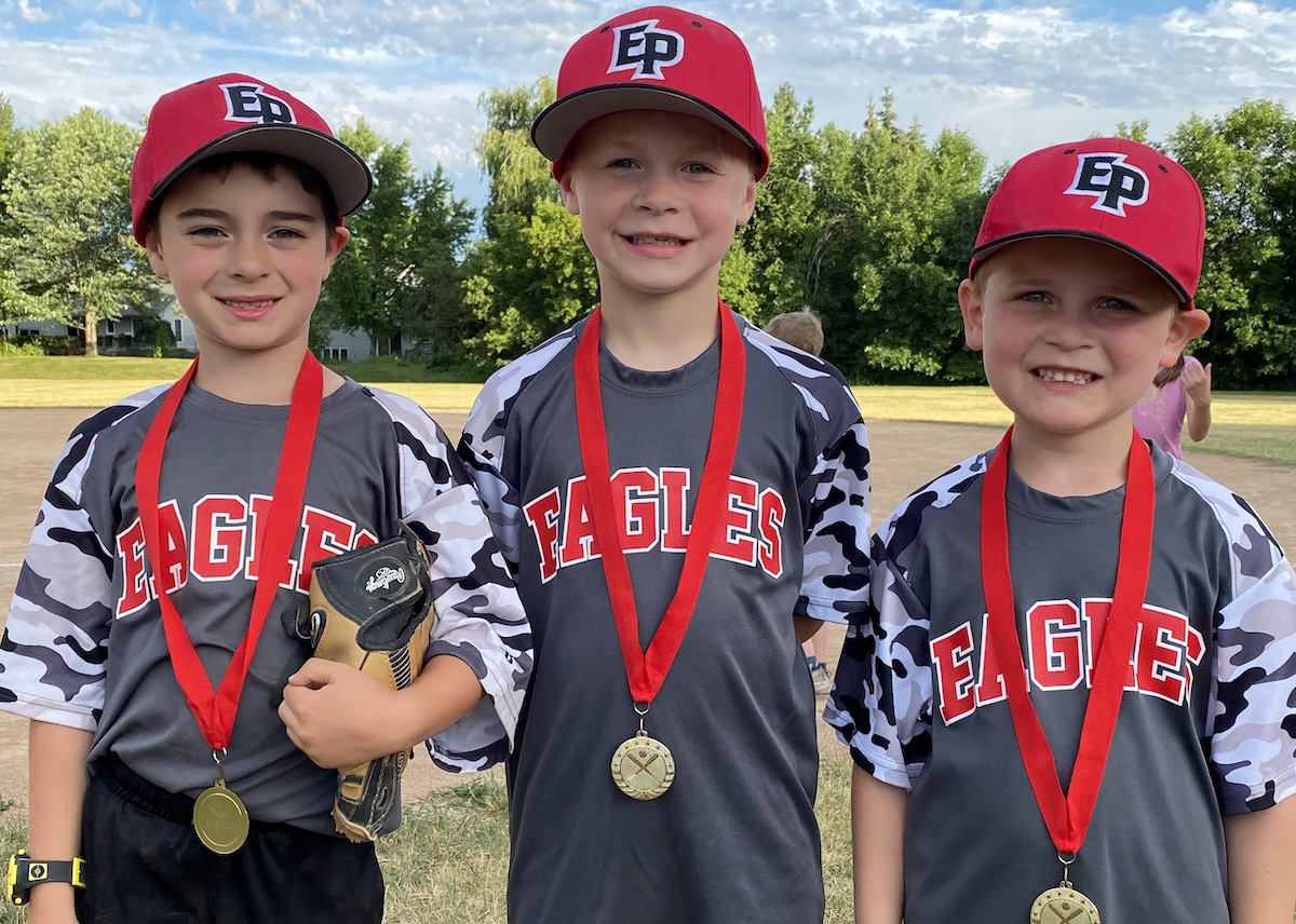 Three young smiling baseball players. The Eden Prairie Baseball Association is offering its Rookie Camp free of charge this year, introducing young children to the fundamentals of the game.