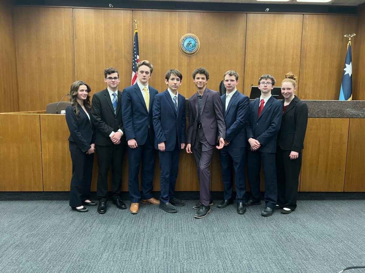 8 young people wearing suits stand in front of U.S. and Minnesota flags, Minnesota state seal