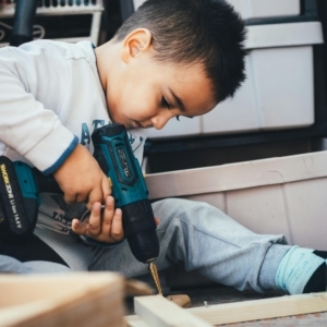 A young boy using a drill on wood.