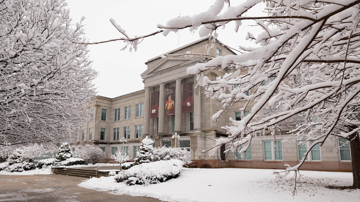 snow-covered trees and lawn in front of large building with columns