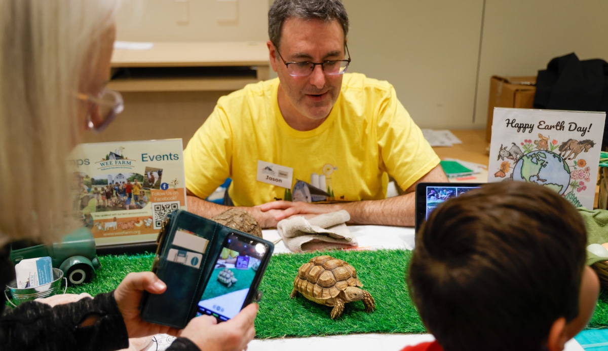 man in yellow shirt watches tortoise crawl on table as little boy looks on
