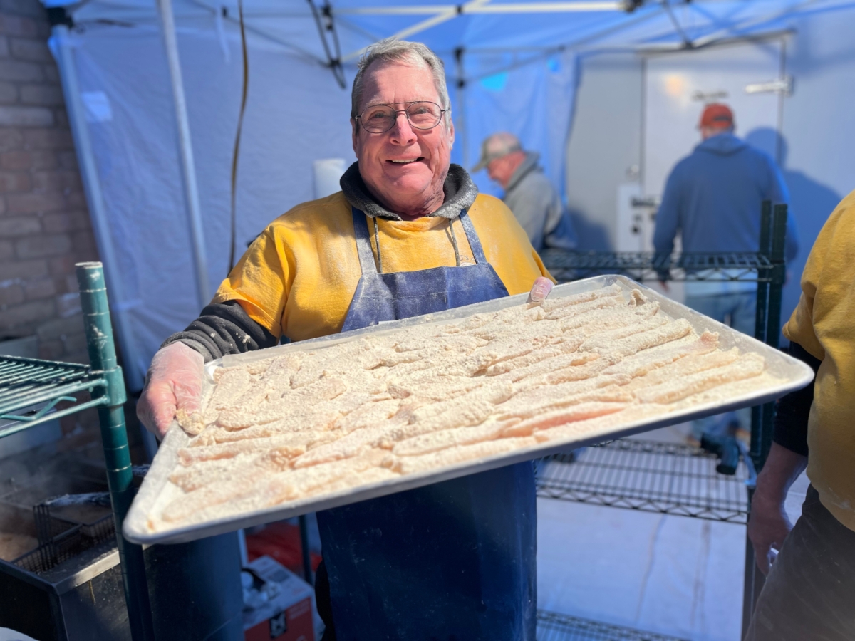 smiling man holds large tray of uncooked fish fillets under outdoor tent