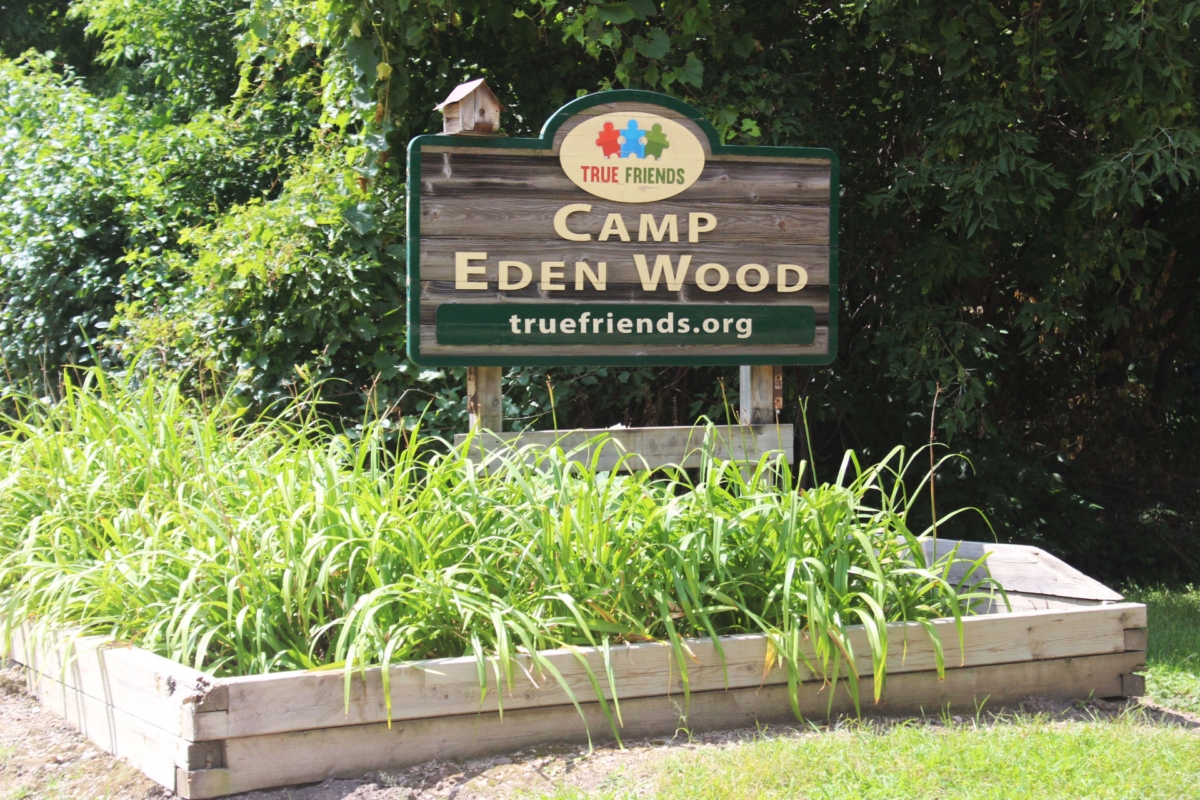 wooden sign saying Camp Eden Wood among green vegetation