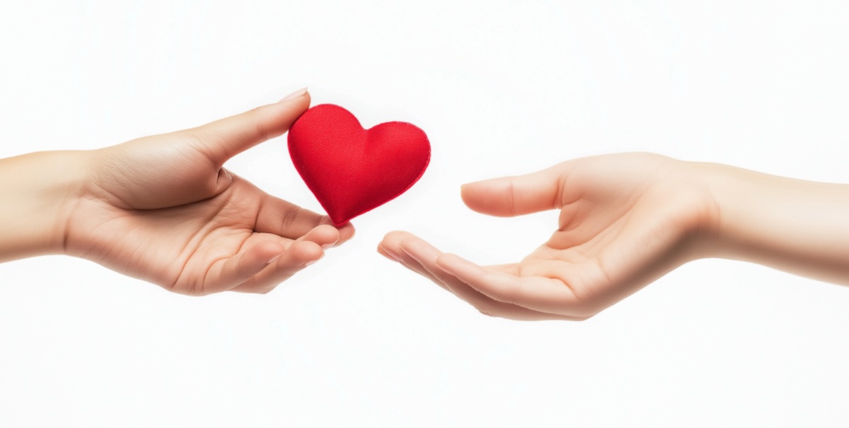 A photo illustration of someone one person handing a heart to another. All you can see are two hands and the heart.