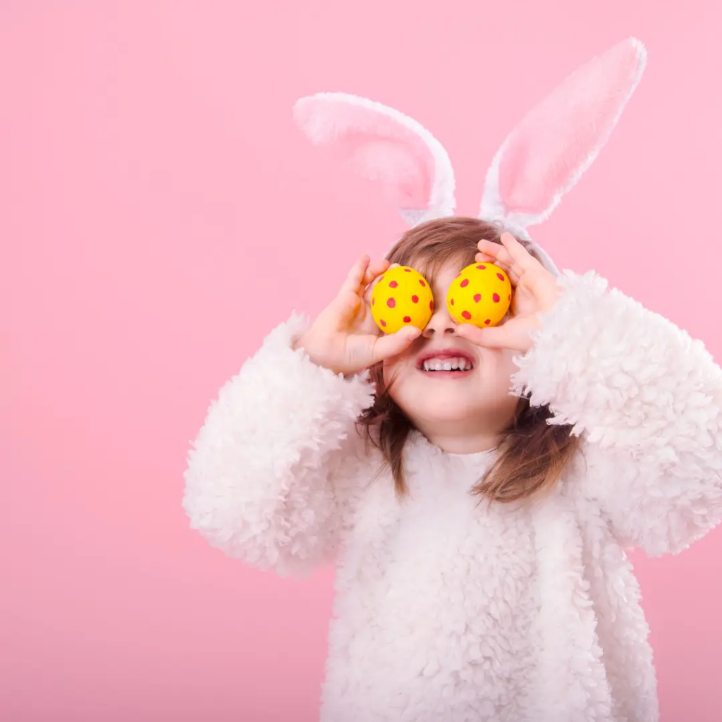 A little girl in a bunny costume holding decorated Waster eggs in front of her eyes.