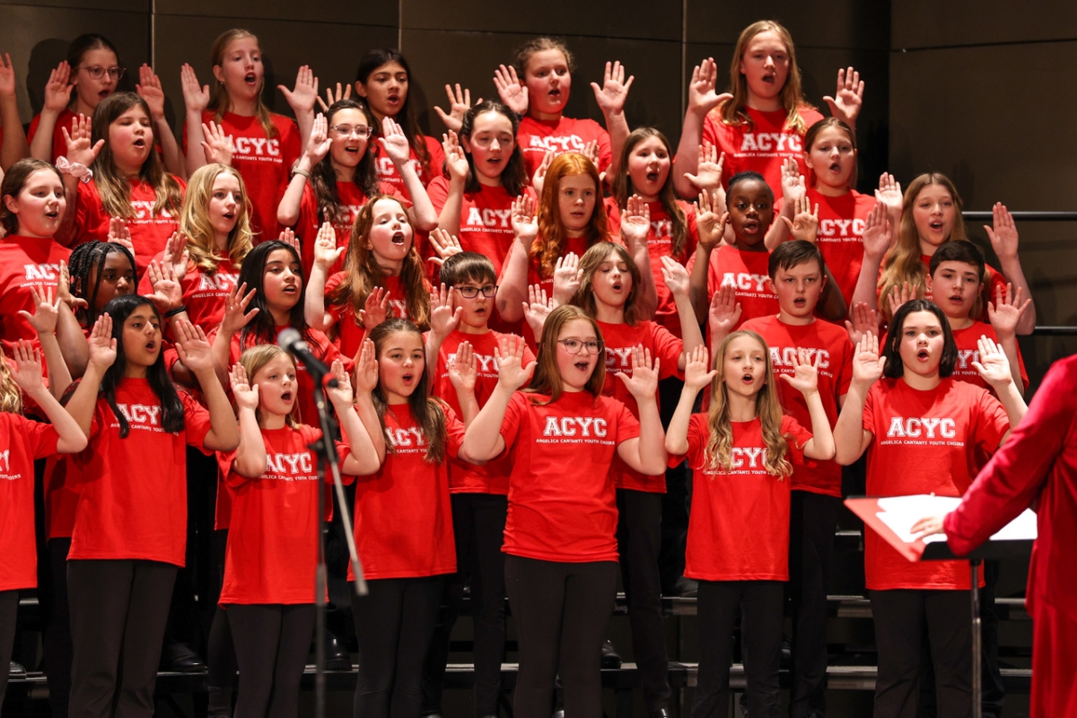 group of Angelica Cantati Cantabile choir singers in red T-shirts with both hands raised