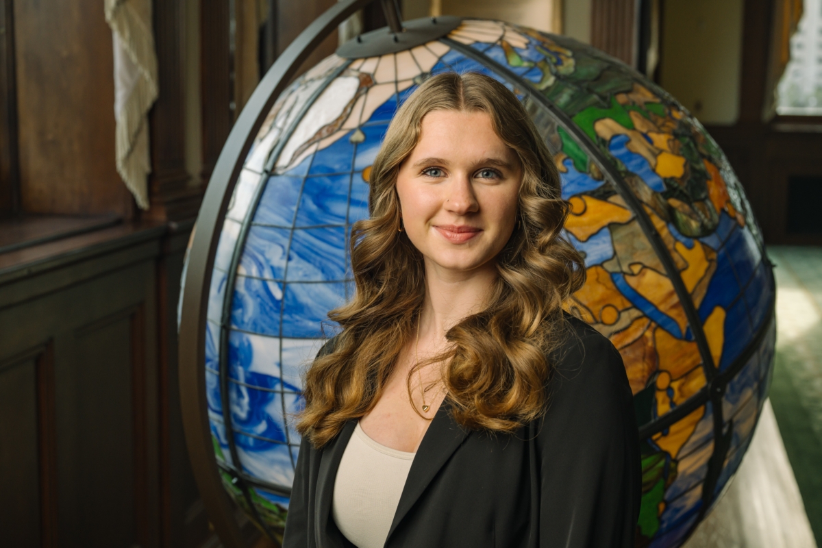 young woman in dark blazer standing in front of oversized globe