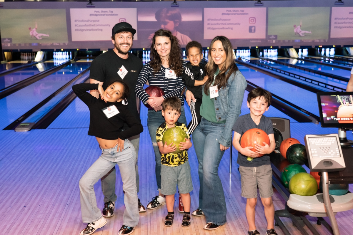 adults and children posing in front of a bowling lane while holding bowling balls