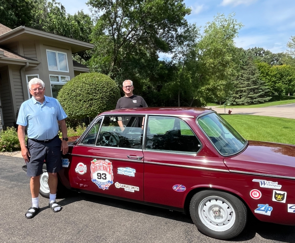 2 men stand next to dark red 1973 BMW 2002 in driveway