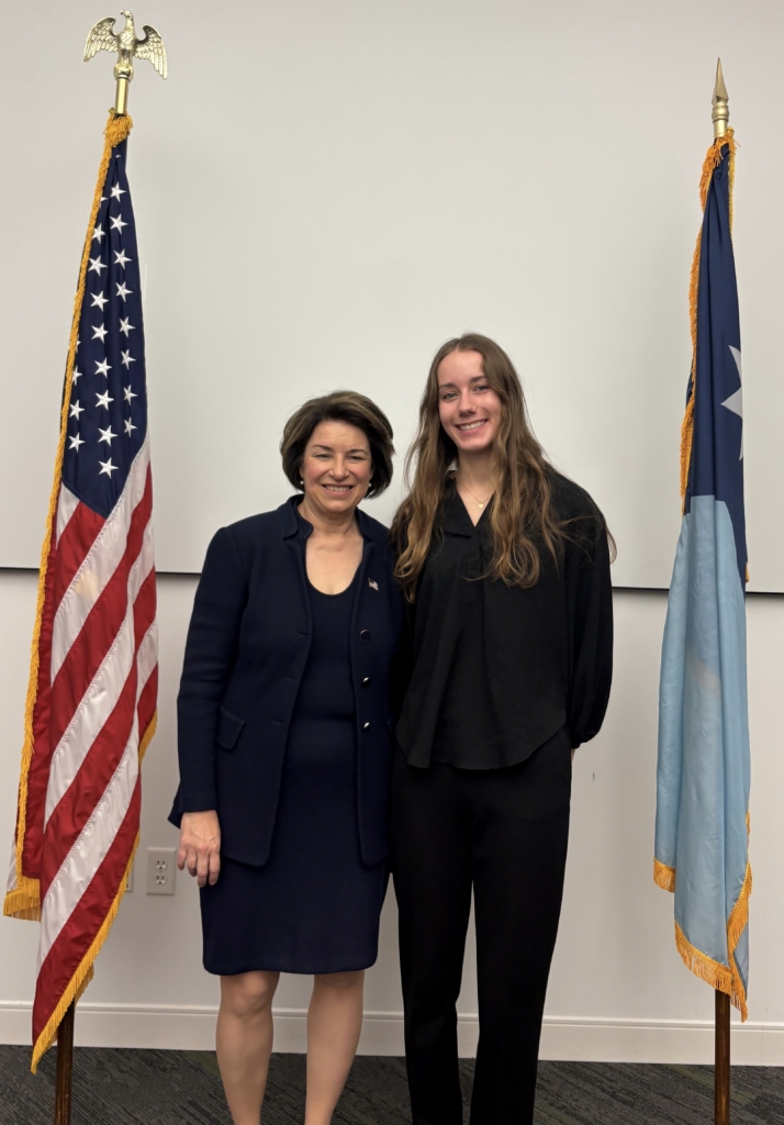 2 women stand between U.S. and Minnesota flags