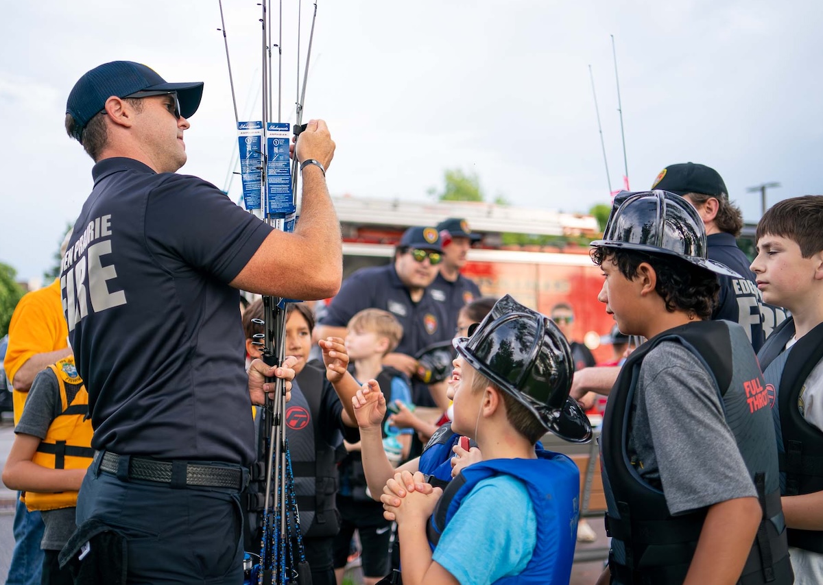 Eden Prairie firefighter C. Curtis hands out fishing rods to young participants at the Hooks and Ladders youth fishing event on June 30 at Riley Lake Park. Each child received a rod, courtesy of Scheels, before boarding a pontoon with local firefighters for an evening of catch-and-release fishing. Photo by Hayden Koughan