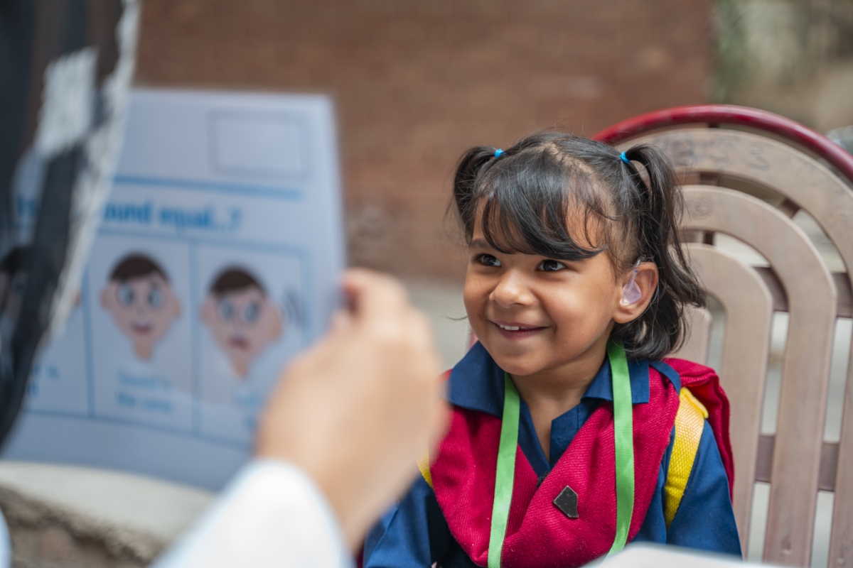 little girl smiles while testing hearing aids with help of audiologist