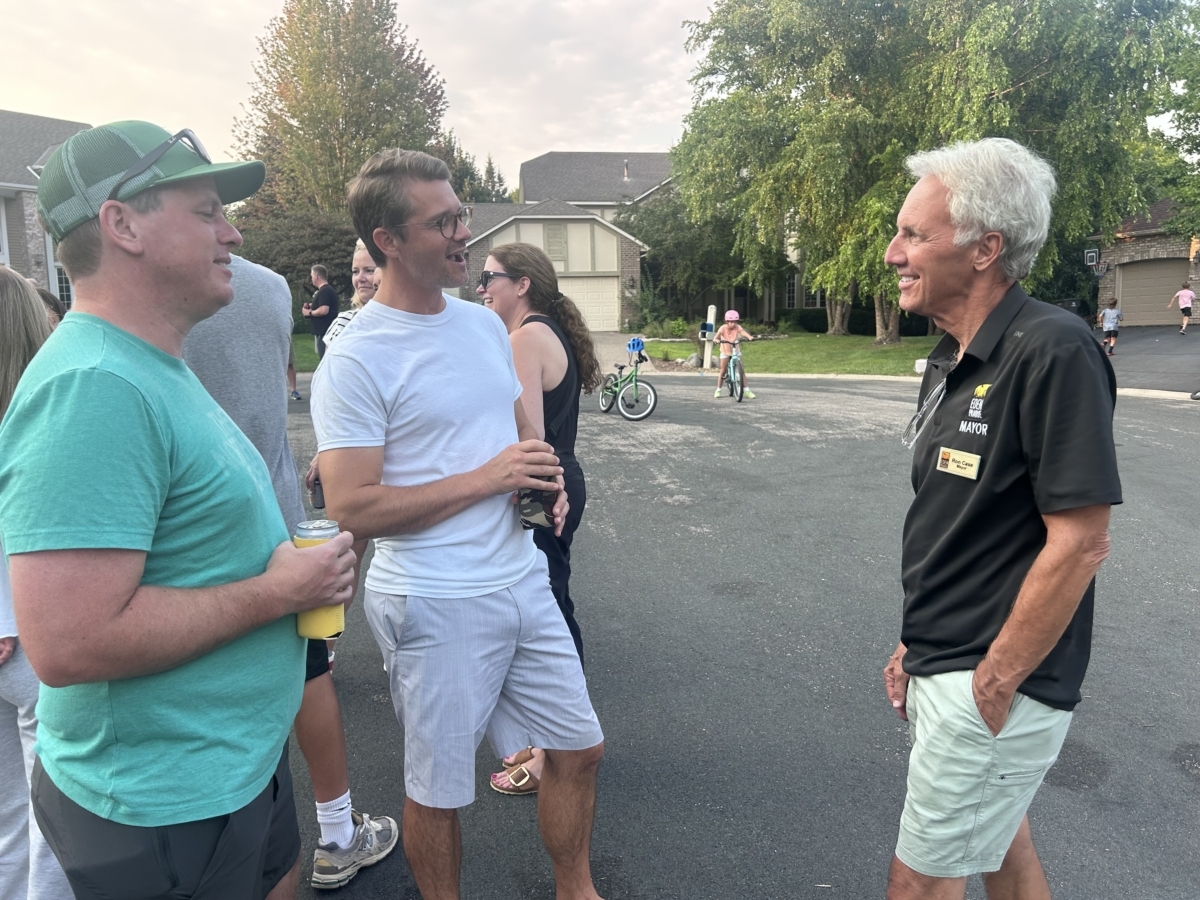 Three men converse in a cul-de-sac. Two of the men are holding canned drinks.