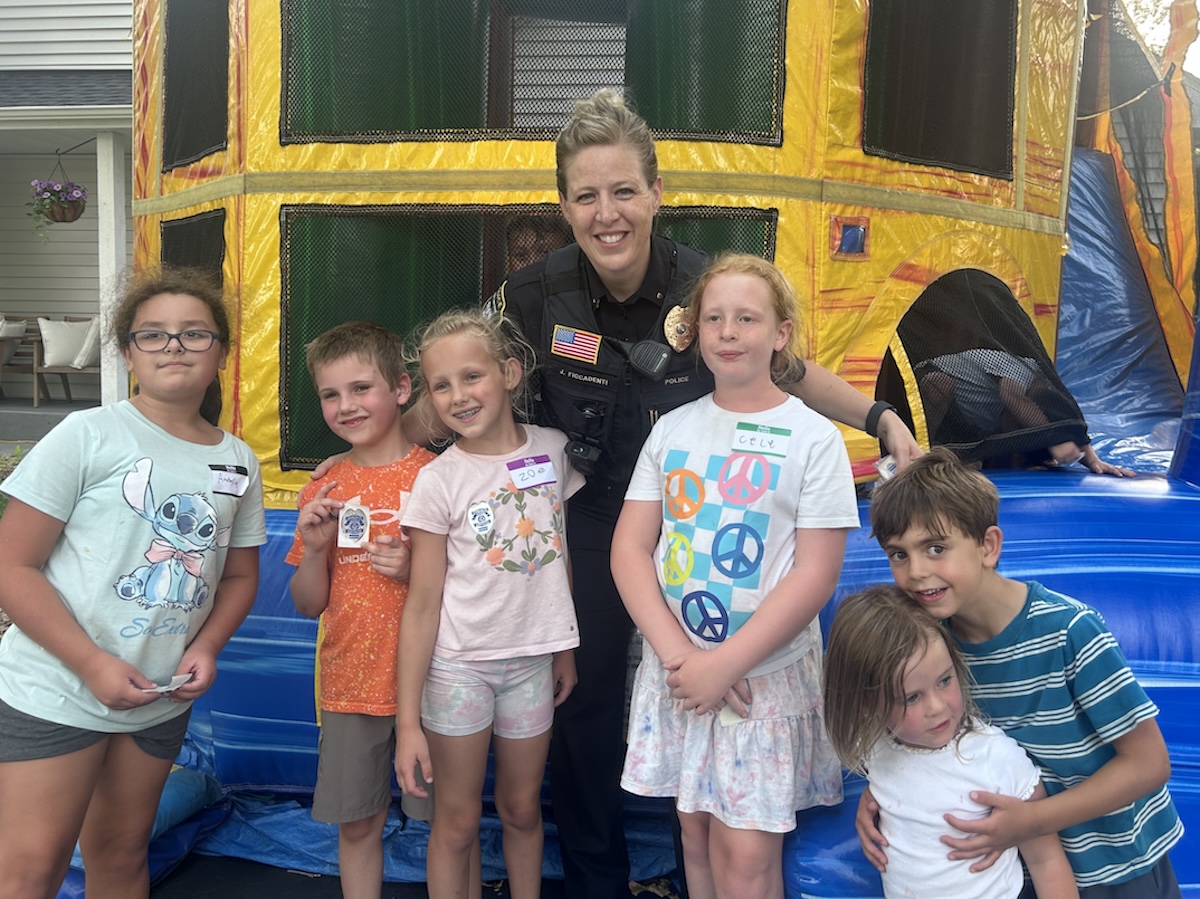 A group of children smile for a picture with a police officer in front of a bounce house.