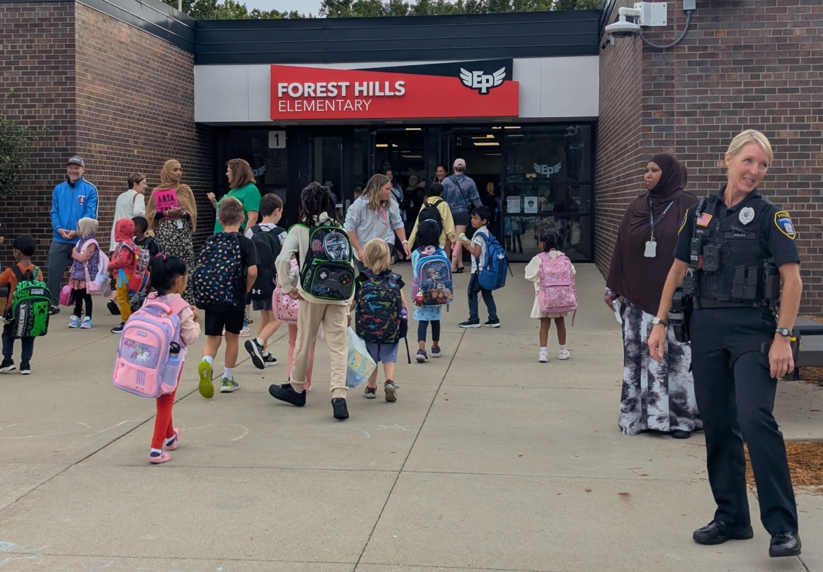 Elementary school students walking through the front door of Forest Hills Elementary School. Parents, teachers and other school officials are assisting them inside.
